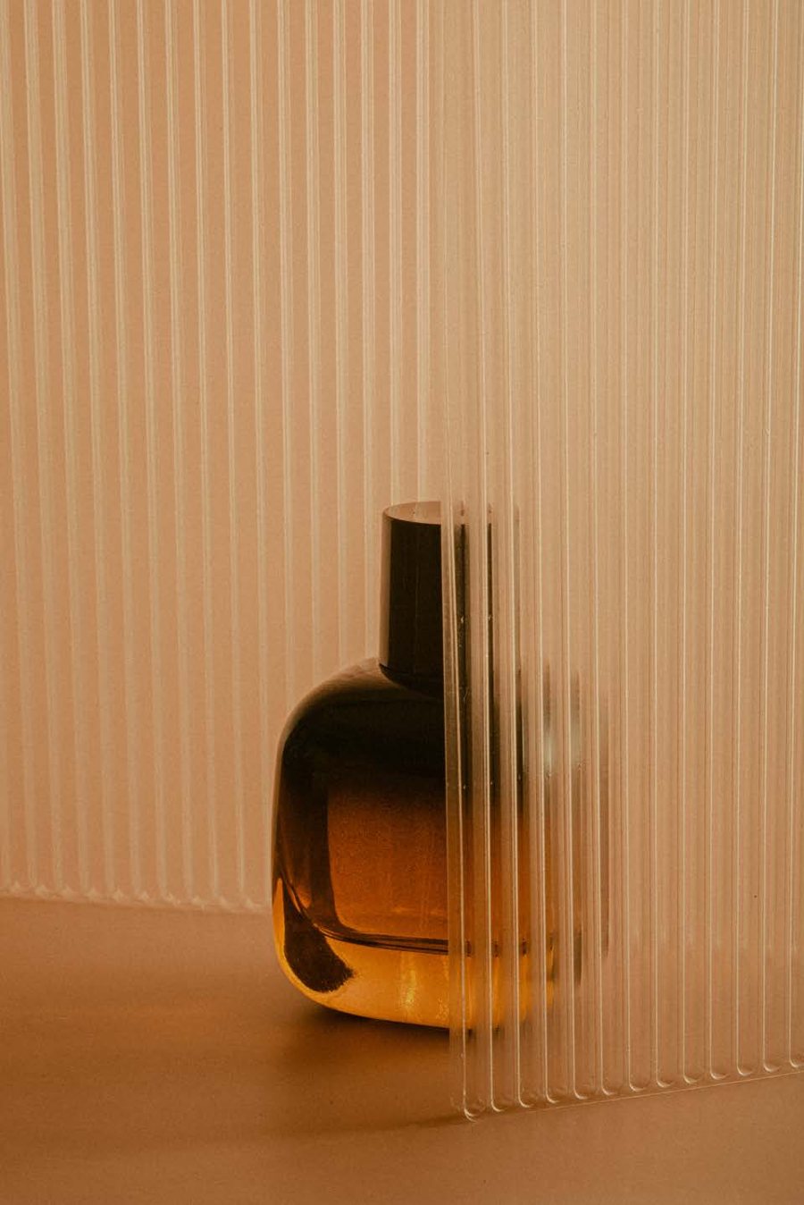An amber VÉYAN fragrance bottle behind fluted glass