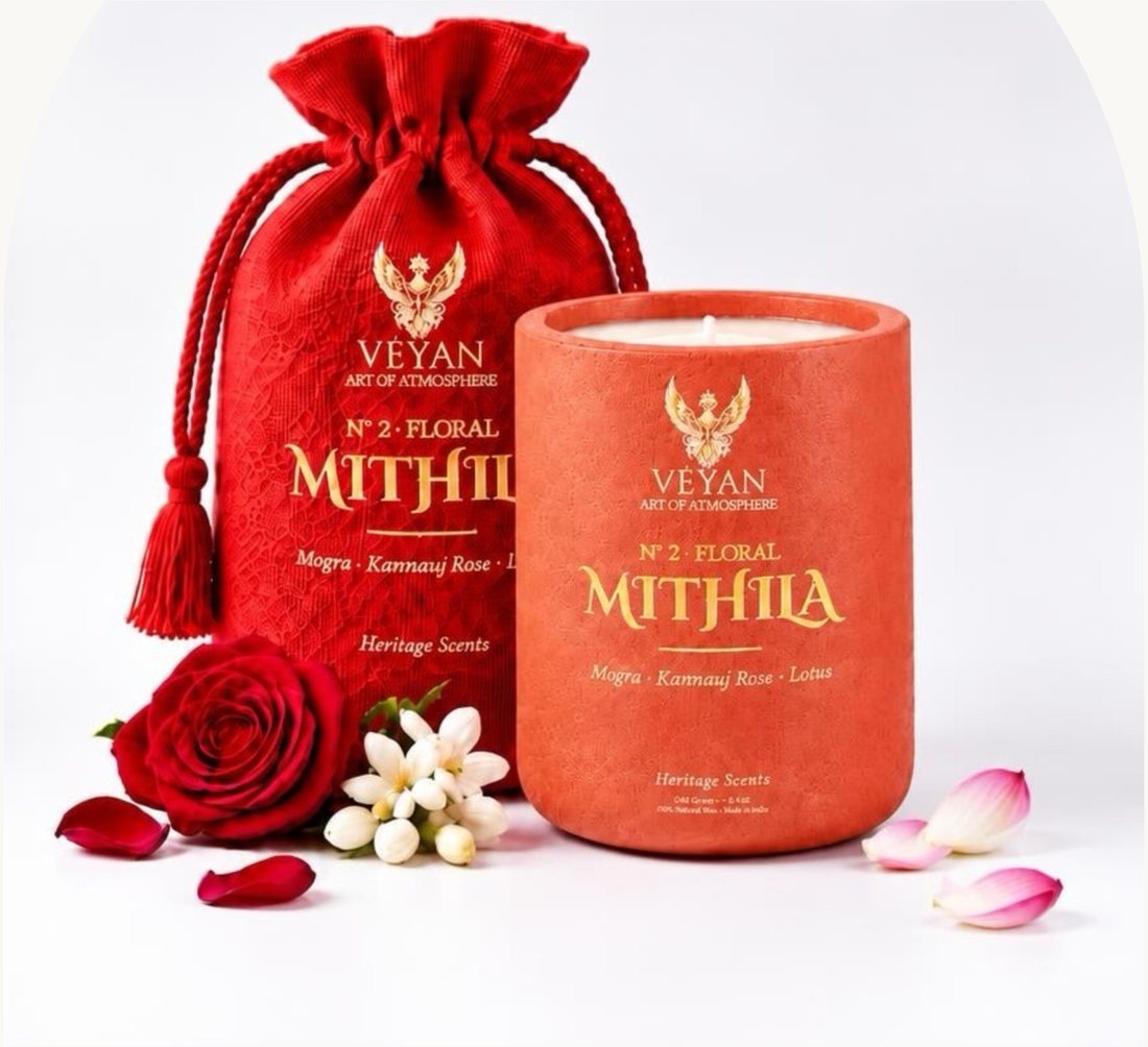 Mithila Heritage Scent candle in a coral vessel beside its red potli, with rose and jasmine